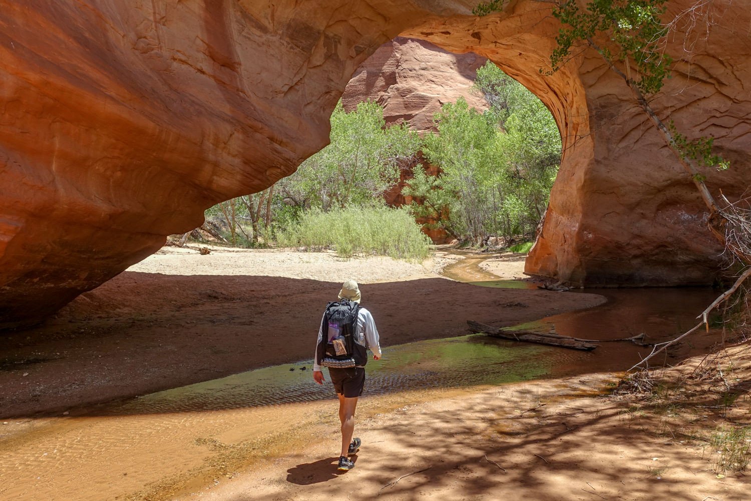 A backpacker hiking through a natural arch in Coyote Gulch