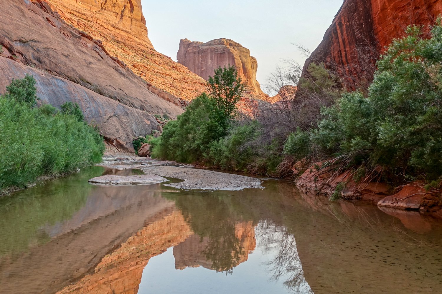 A red rock monolith reflecting in the water at Coyote Gulch