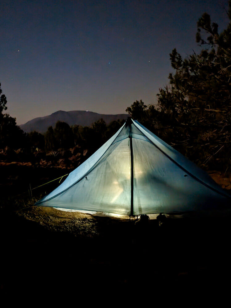 A Zpacks Duplex Zip tent in the dark lit by a headlamp from the inside with stars shining above in the sky 