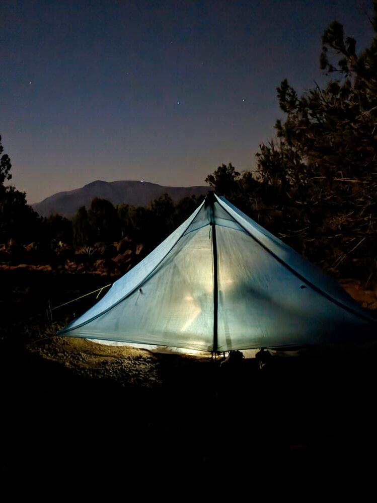 A Zpacks Duplex Zip tent in the dark lit by a headlamp from the inside with stars shining above in the sky