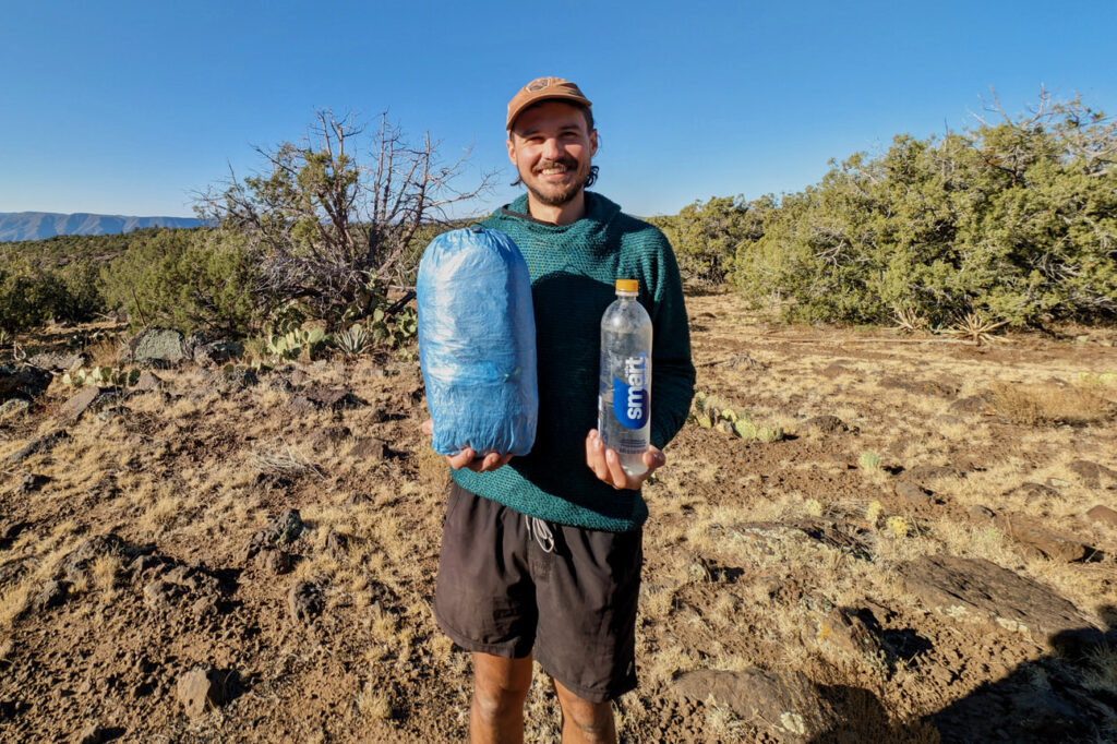 A hiker holding the Zpacks Duplex Zip tent in one hand and a water bottle in the other hand to show the size of the packed tent