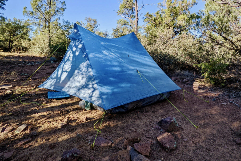 The Zpacks Duplex Zip tent set up among trees with red dirt in the foreground and shadows across the tent