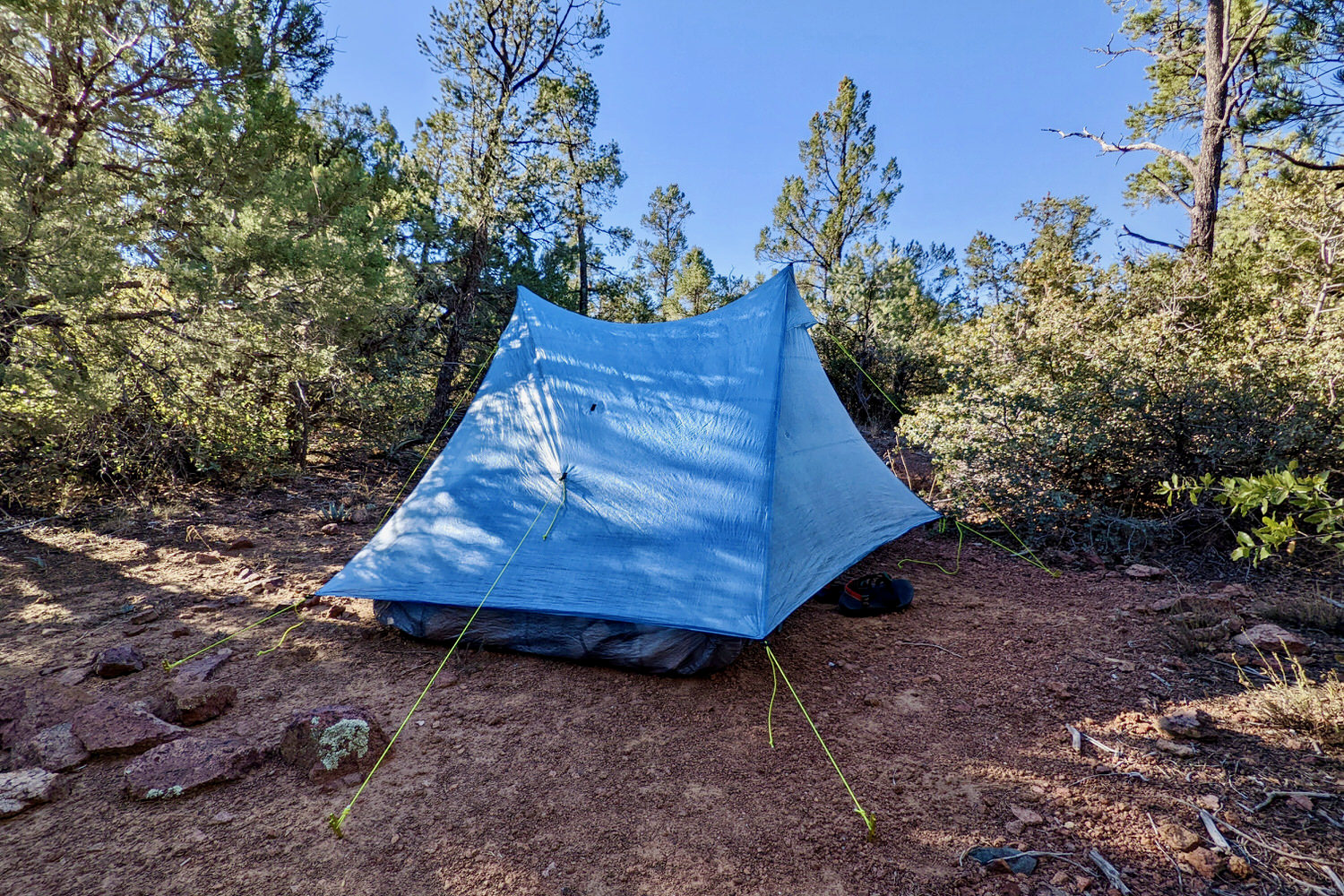 The Zpacks Duplex Zip tent set up among trees with red dirt in the foreground and shadows across the tent 