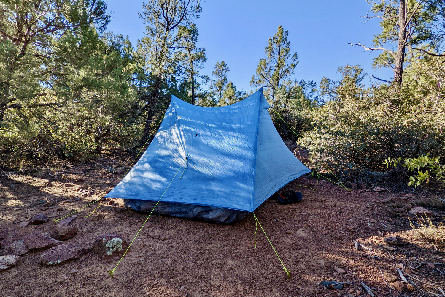 The Zpacks Duplex Zip tent set up among trees with red dirt in the foreground and shadows across the tent