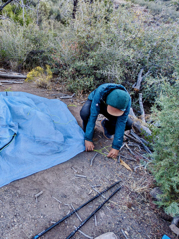 A hiker securing the tent steaks on the Zpacks Duplex Zip tent with a view of the tent flat on the ground  
