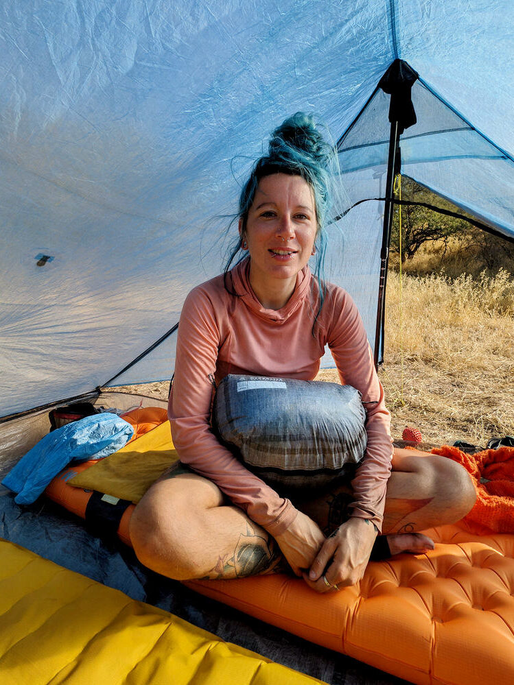 A hiker sitting inside the Zpacks Duplex Zip tent smiling at the camera with a stuff sack on her lap