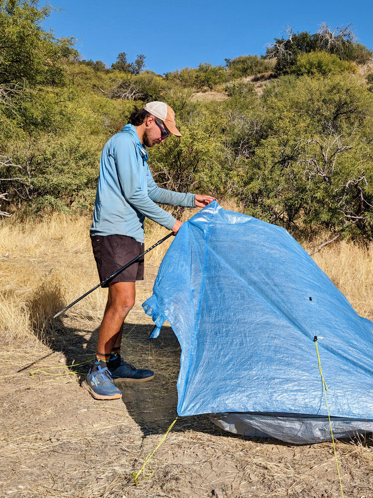 A hiker setting up the Zpacks Duplex Zip tent using trekking poles to prop up one side of the tent 