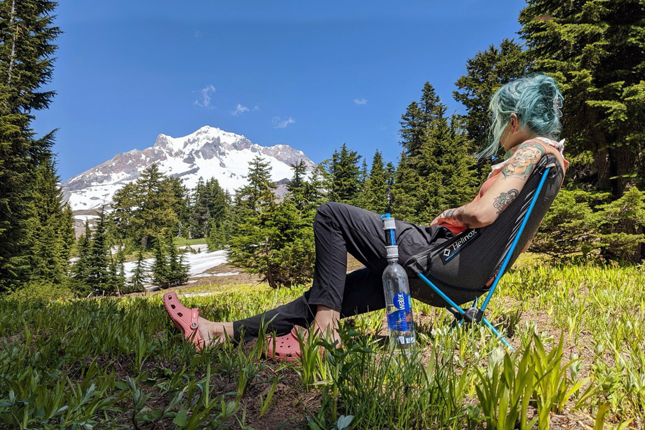 A backpacker relaxing in the Helinox Chair Zero in an alpine meadow view a view of a snowy mountain
