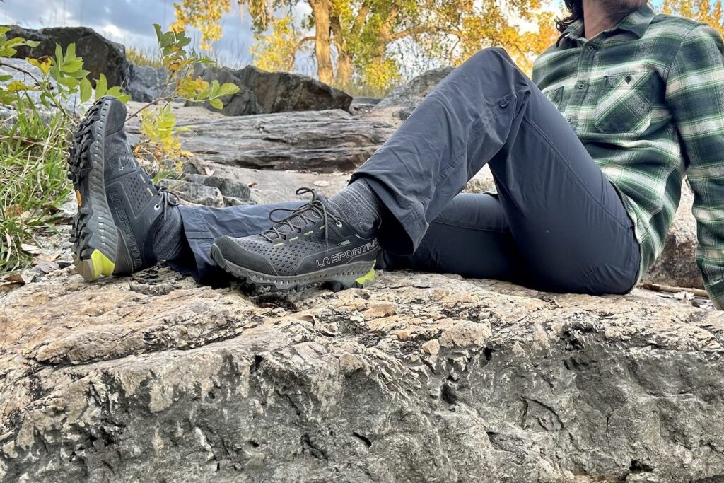 The lower half of a male hiker sitting on a rocky slab in hiking pants and the La Sportiva Spire GTX hiking shoes