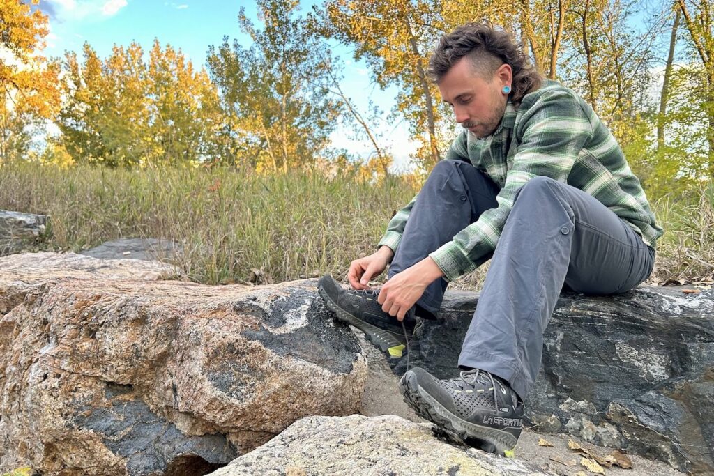 Full-body shot of a hiker sitting down on rocks to tie the La Sportiva Spire GTX hiking shoes