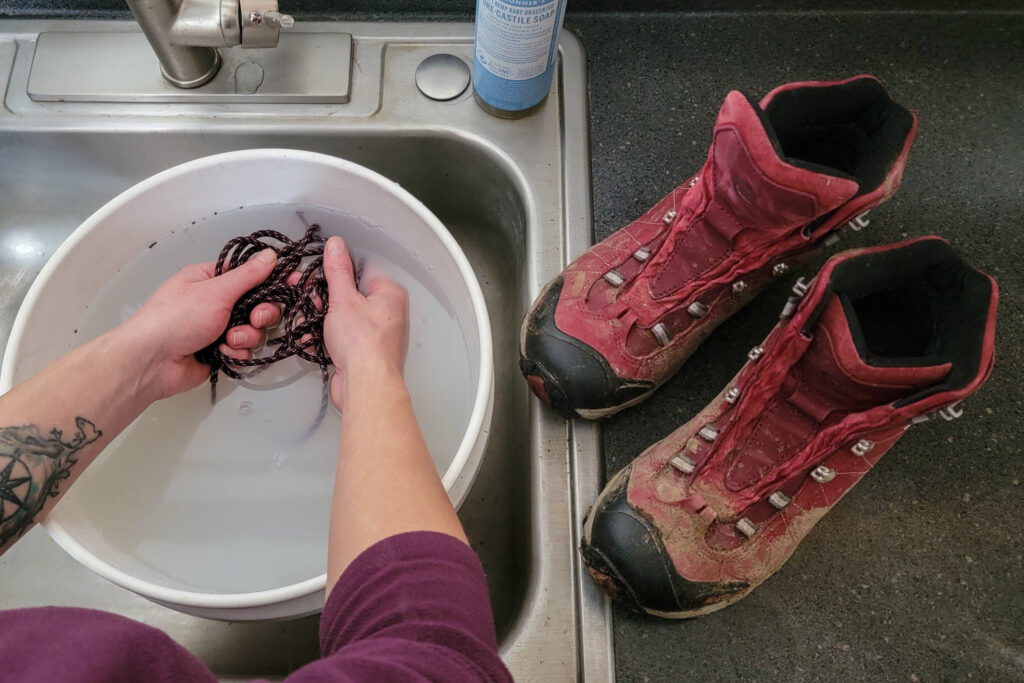 Looking over a woman's shoulder while she washes the laces of her Obōz Bridger hiking boots in a bucket of soapy water