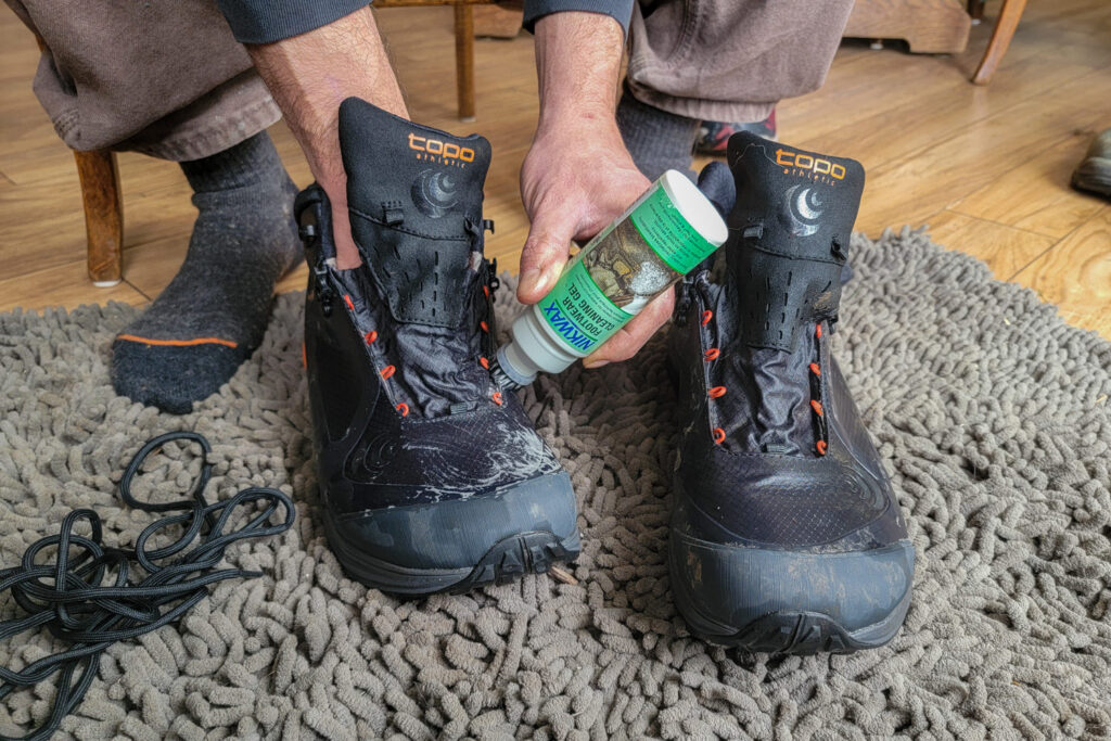 A hiker applying Nikwax Footwear Cleaning Gel to their damp Topo Athletic Trailventure 2 shoes with laces removed