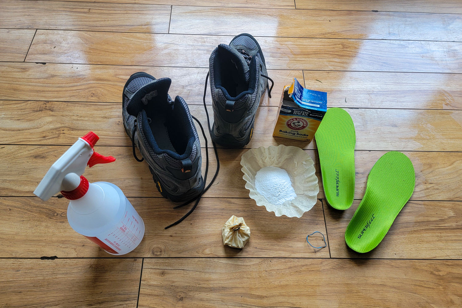 Looking down at a pair of Merrell Moab boots with a spray bottle full of diluted white vinegar, coffee filters filled with banking soda, and a pair of Superfeet insoles