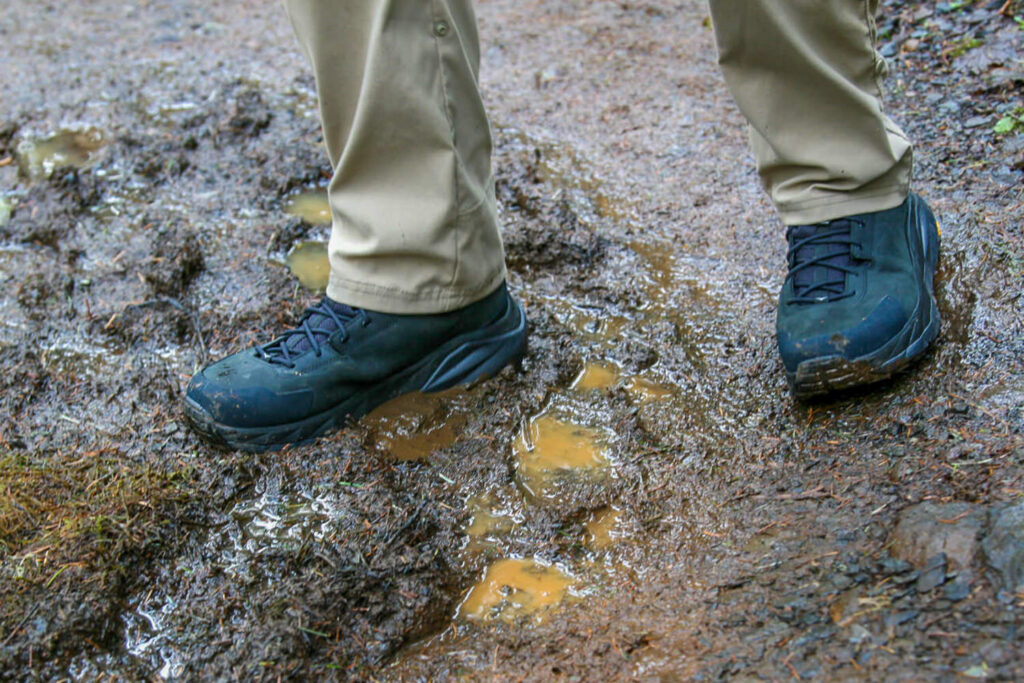 Closeup of a hiker walking down a muddy trail in the HOKA Anacapa 2 Mid GTX boots