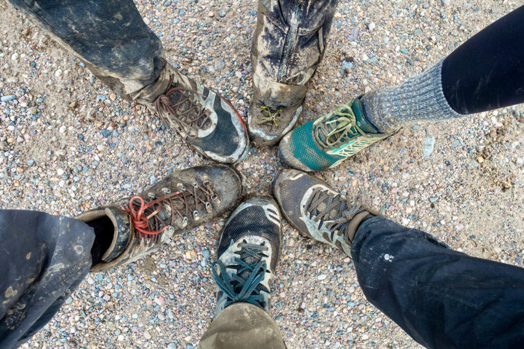 Looking down a a circle of muddy hiking shoes and boots