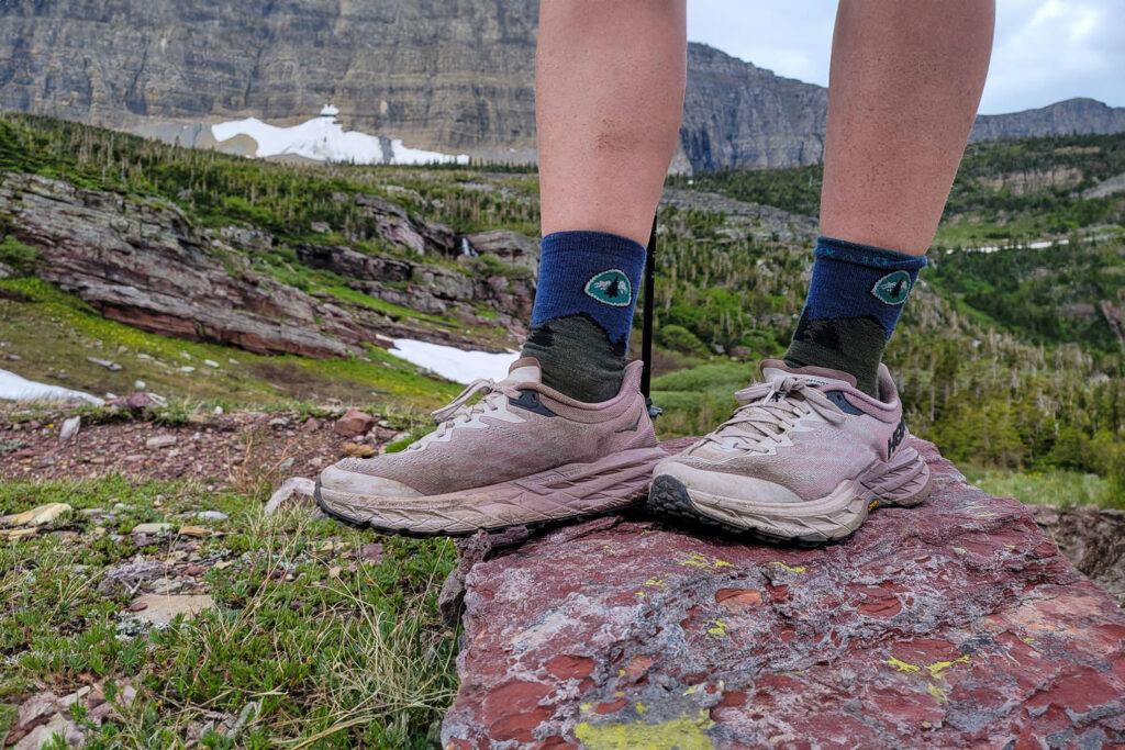A hiker standing on a red rock in Glacier in the HOKA Speedgoat 5 hiking shoes