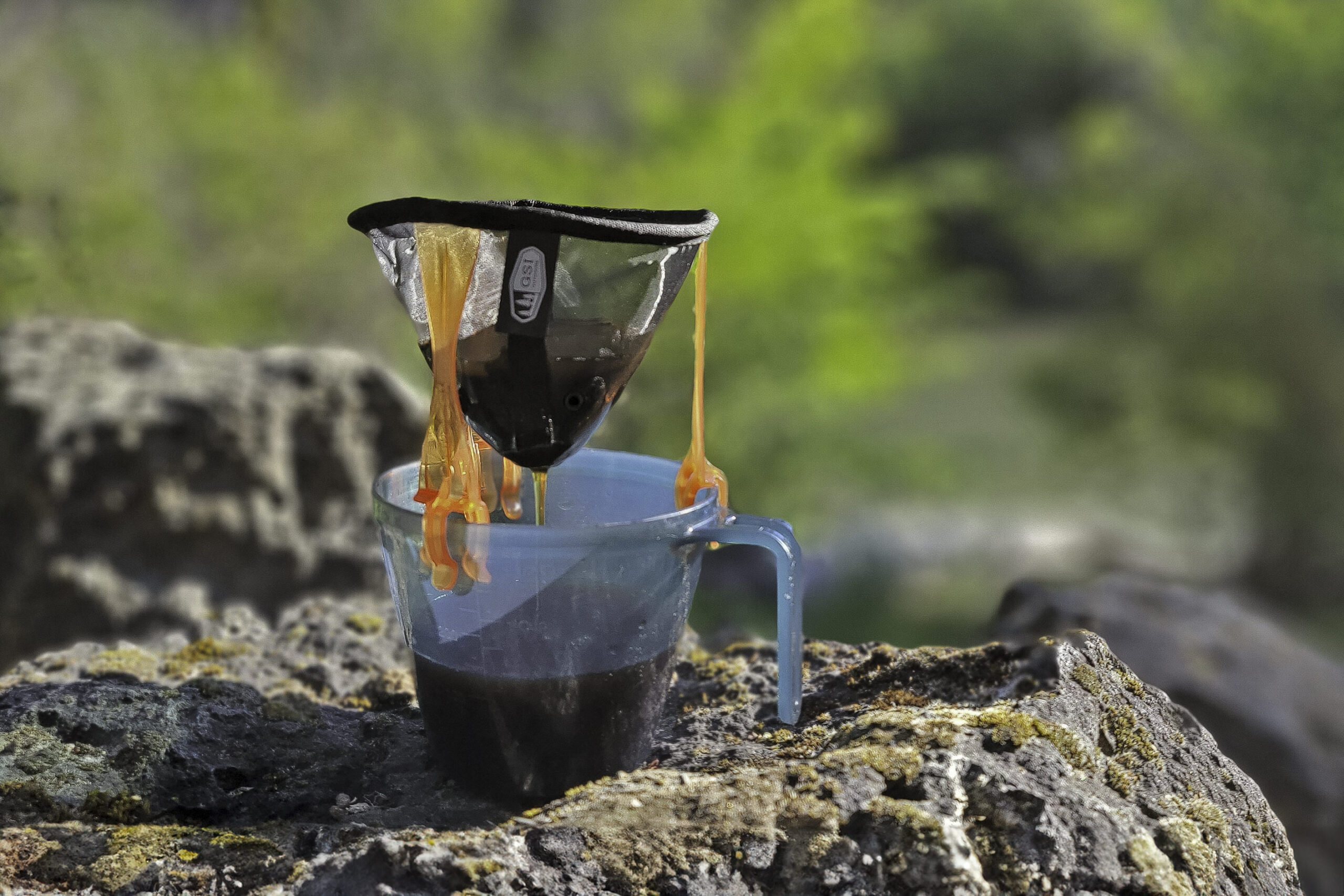 Closeup of the GSI Outdoors Ultralight Java Drip brewing coffee into an ultralight backpacking cup on a volcanic rock