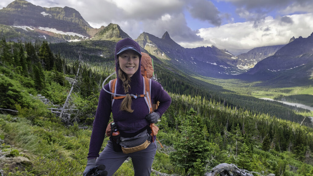 A female backpacker wearing the Eddie Bauer Super Sevens Fleece Pullover in front of jagged mountain peaks in Glacier National Park