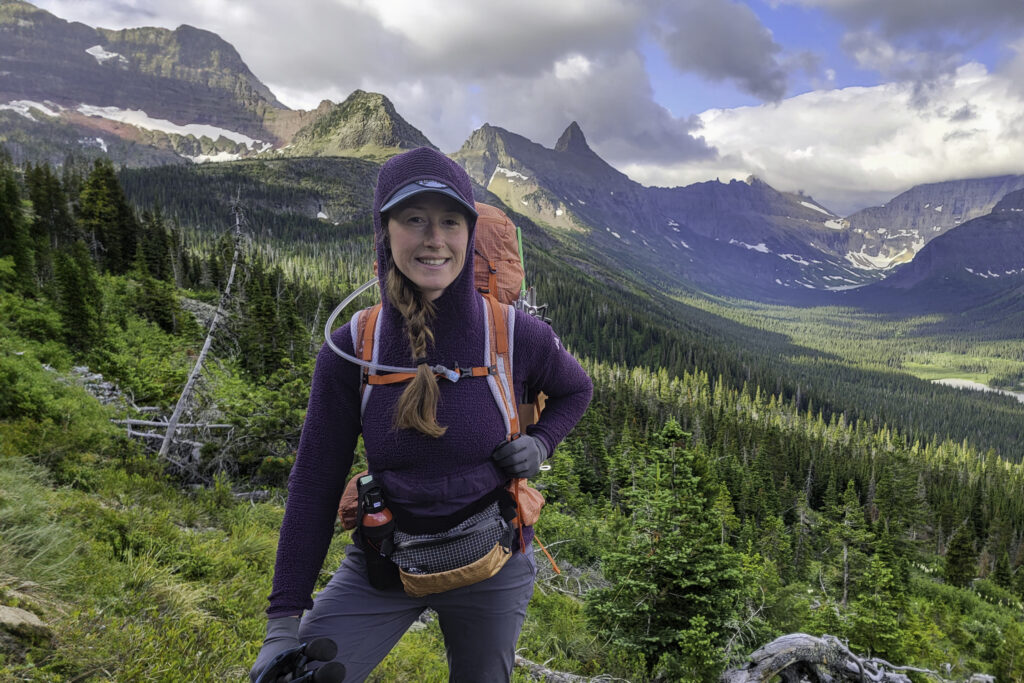 A female backpacker wearing the Eddie Bauer Super Sevens Fleece Pullover in front of jagged mountain peaks in Glacier National Park