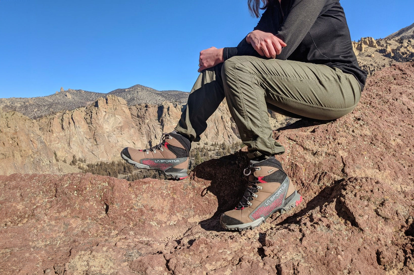 Waist-down view of a hiker taking a rest break by sitting on some rocks in the La Sportiva Nucleo High II GTX boots with rocky, high-desert clifs in the background.