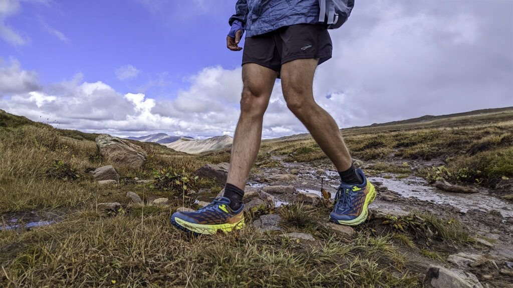 Muscular hiker legs traversing an alpine meadow in the HOKA Speedgoat 5 hiking shoes