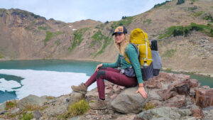 A blonde backpacker sitting on a rock in front of an icey lake in the Fjallraven Abisko Trekking Tights