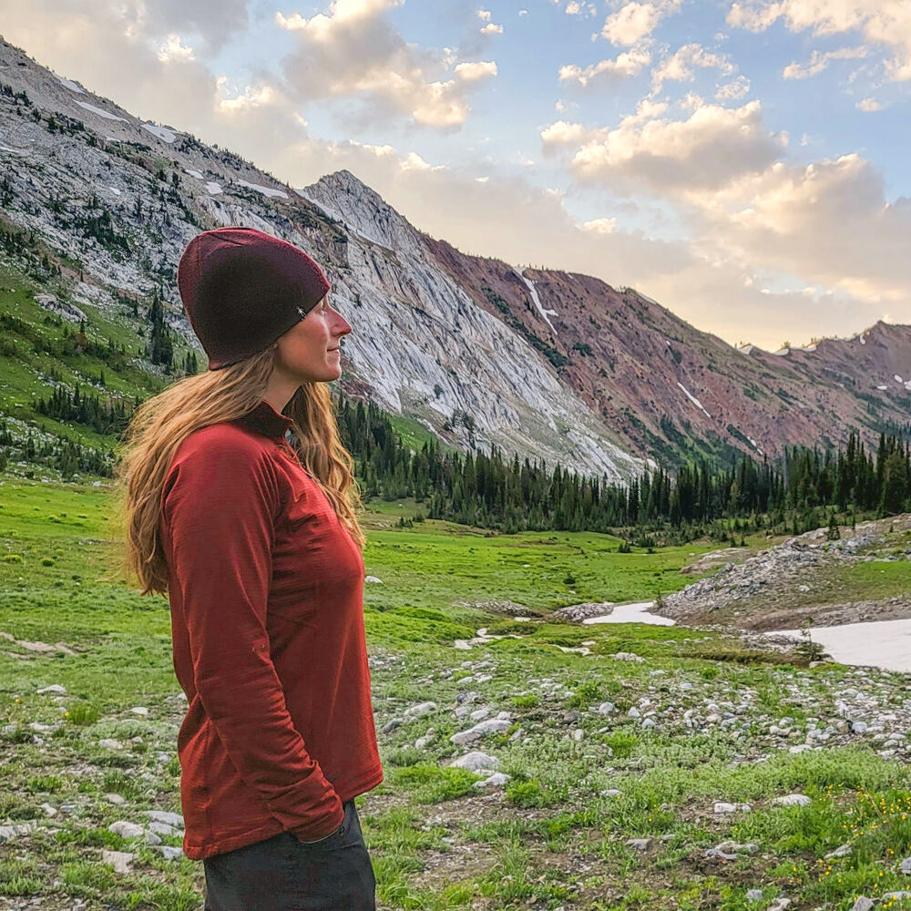 A woman wearing a red Outdoor Research Vigor fleece pullover in a granite mountain-lined valley
