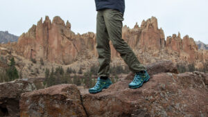 A waist-down photo of a female hiker wearing The North Face Aphrodite 2.0 hiking pants with the tuft columns of Smith Rock in the distance