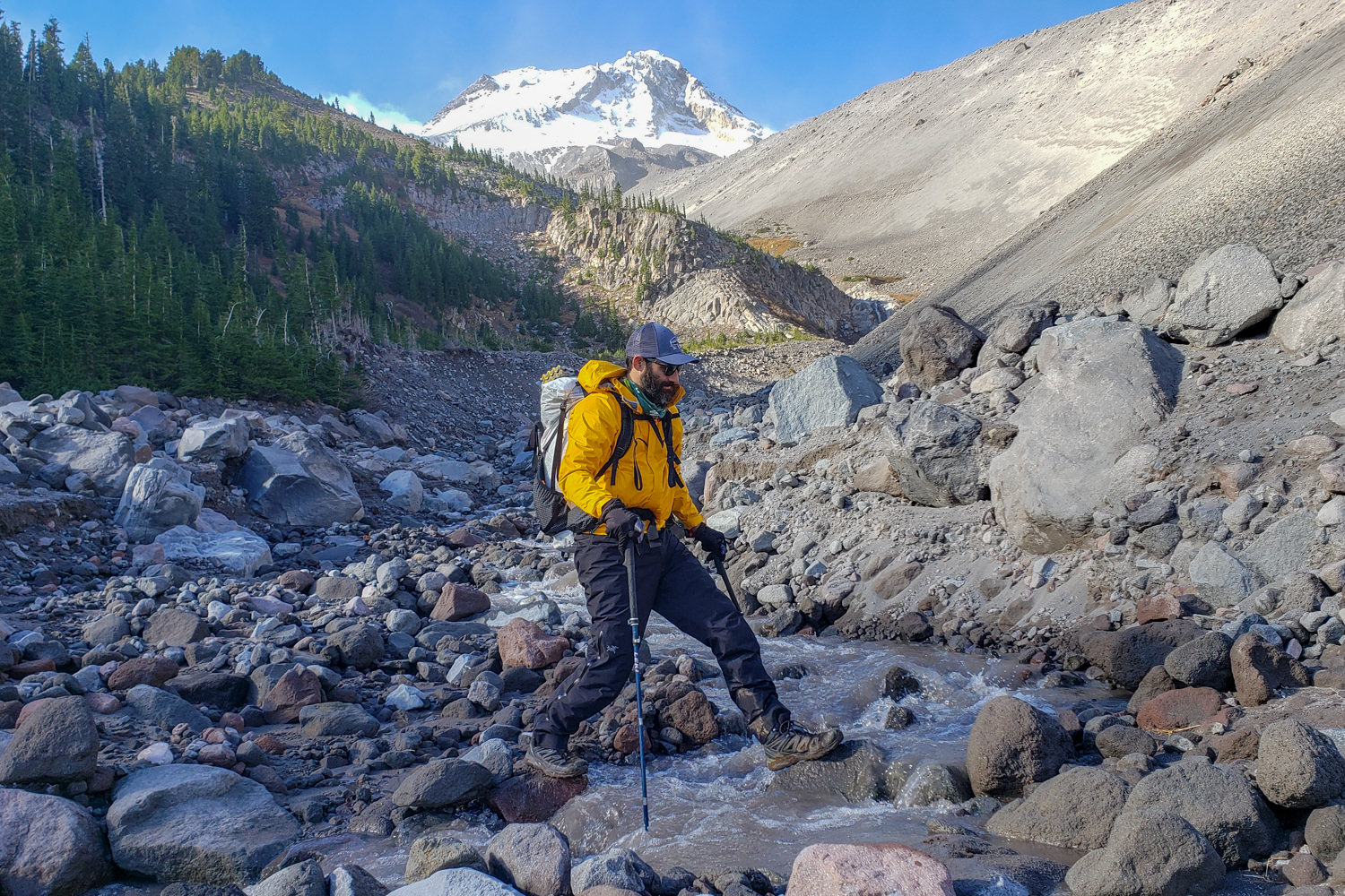 A backpacker crossing a rocky, glacial creek in the Marmot PreCip rain jacket