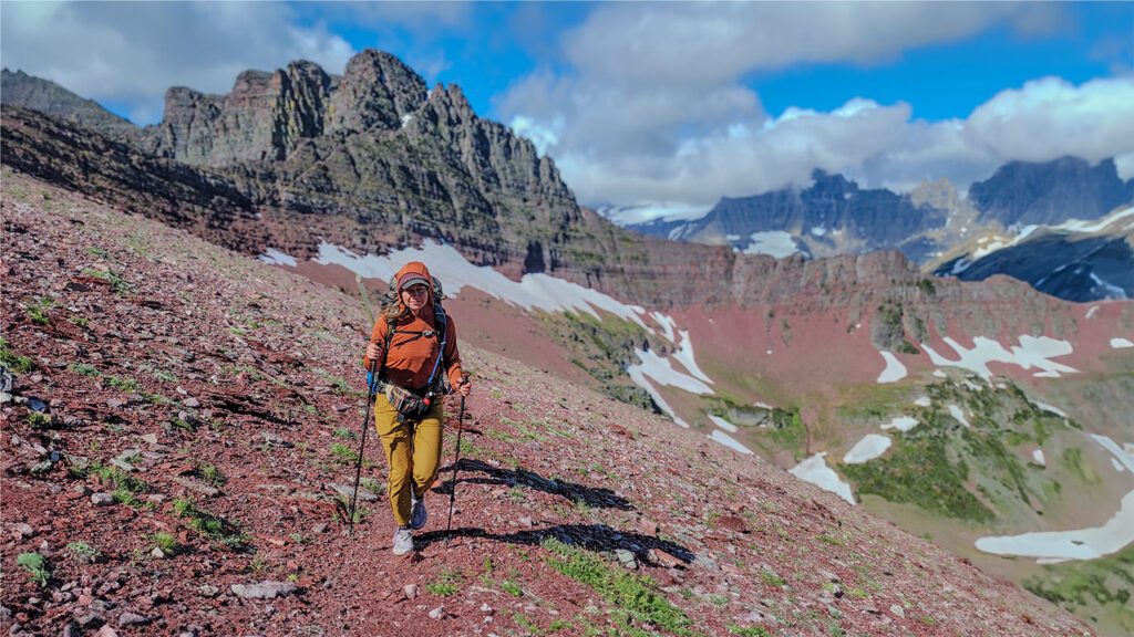 A female backpacker hiking up to the top of a red, rocky mountain pass in Glacier National Park using the REI Flash Carbon trekking poles