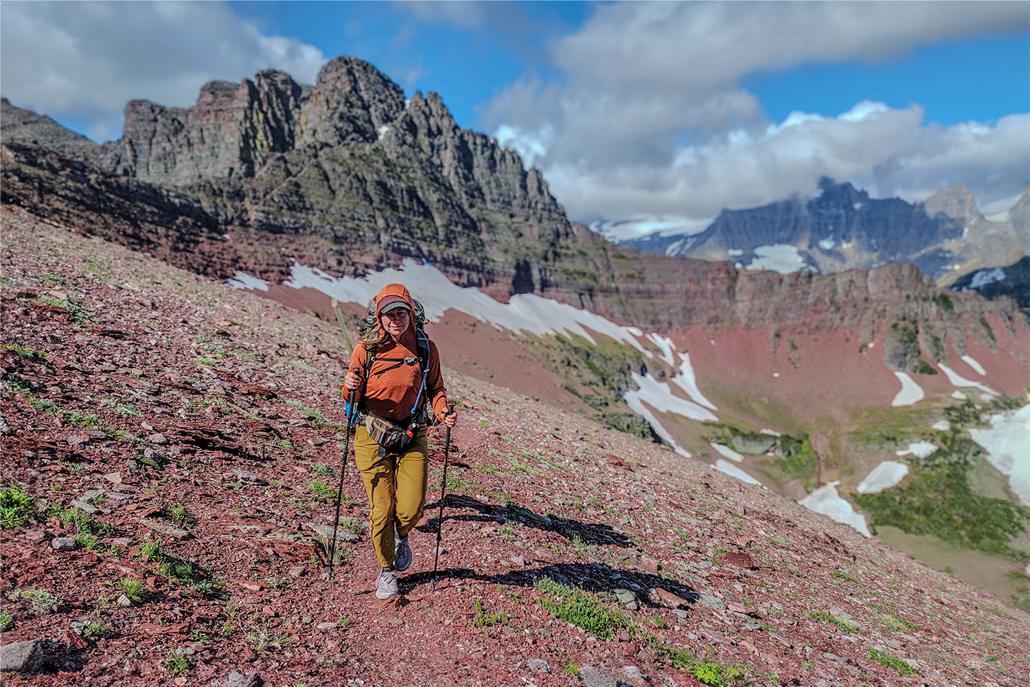 A female backpacker hiking up to the top of a red, rocky mountain pass in Glacier National Park using the REI Flash Carbon trekking poles