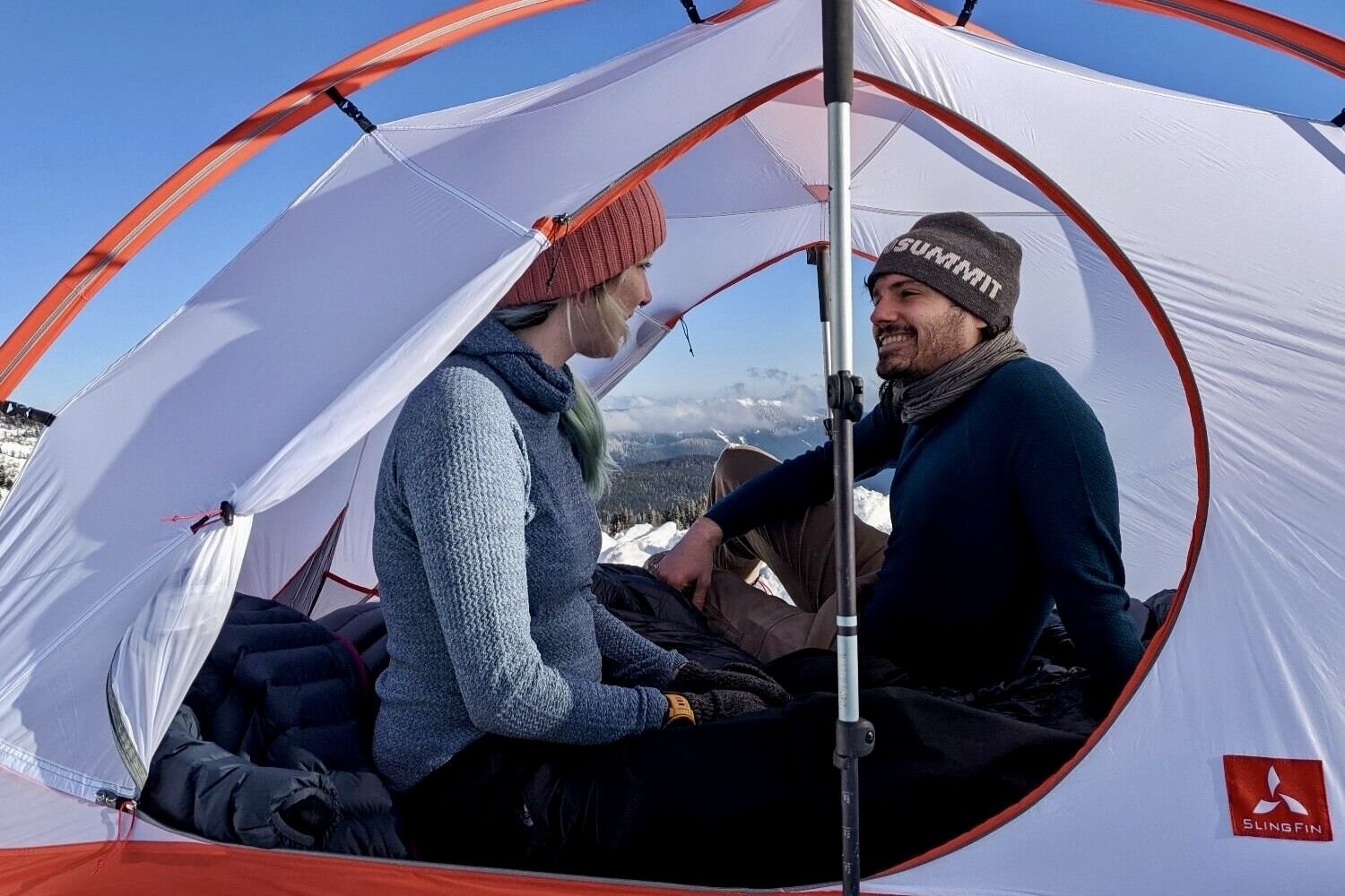 Two hikers sitting in the Slingfin Crossbow tent. The woman is wearing the Patagonia Capilene Air Hoodie