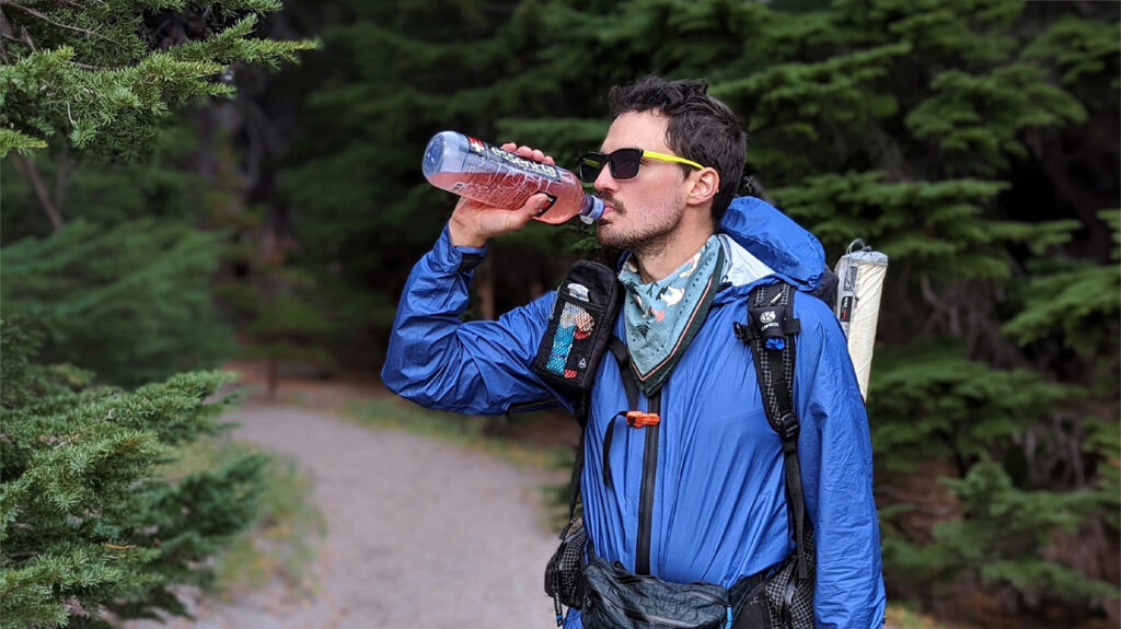 A backpacker drinking from a water bottle filled with pink hydration mix