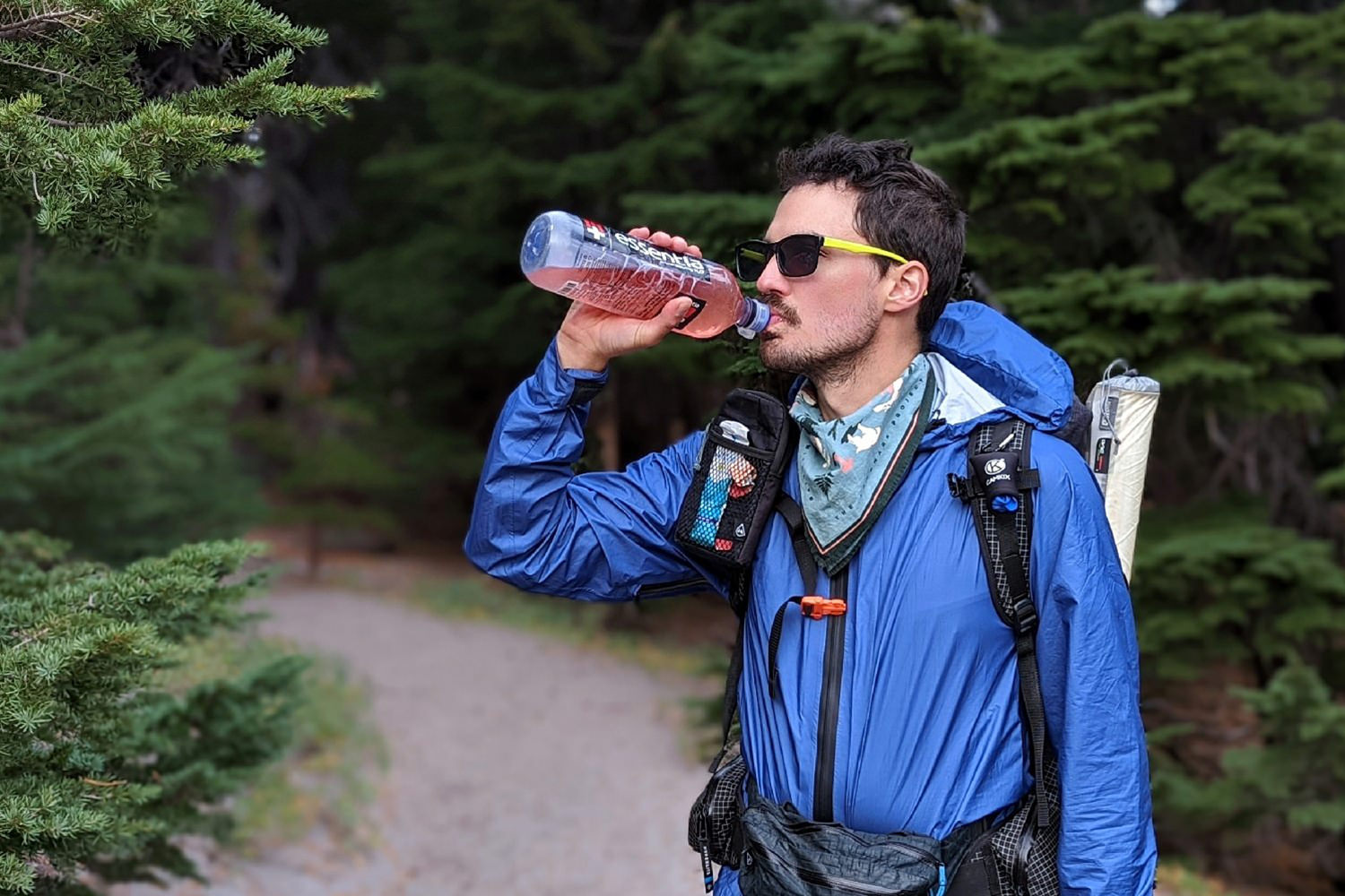 A backpacker drinking from a water bottle filled with pink hydration mix