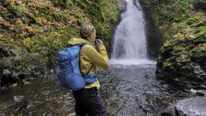 A hiker in front of a waterfall with the Gregory Juno 24 H2O hydration pack