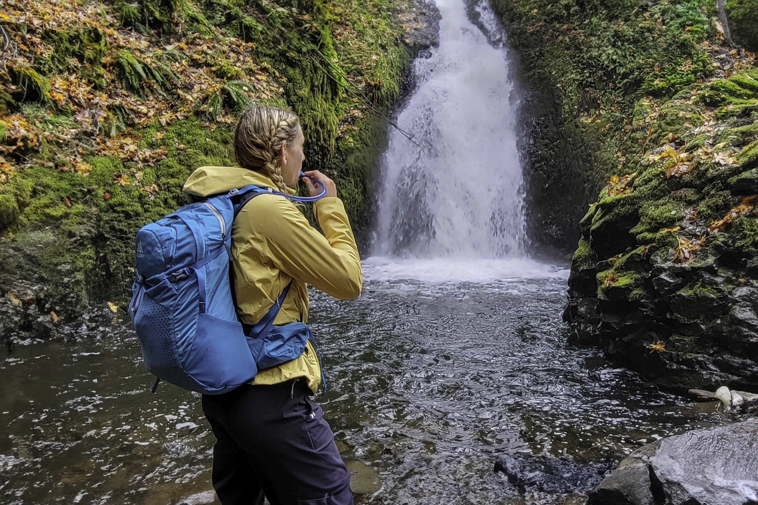 A hiker in front of a waterfall with the Gregory Juno 24 H2O hydration pack