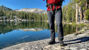 A backpacker standing in front of a lake in the men's Kuhl Deceptr hiking pants
