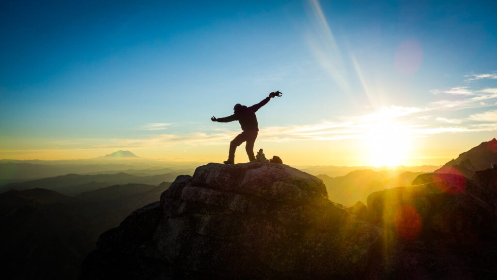 A hiker posing on top of a mountain at sunset