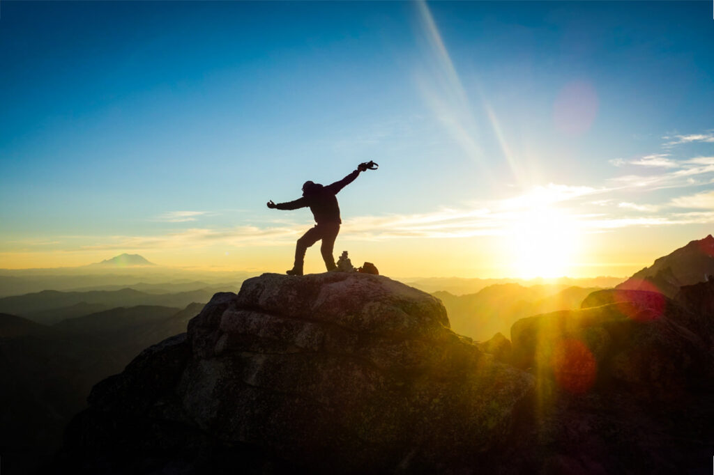 A hiker posing on top of a mountain at sunset