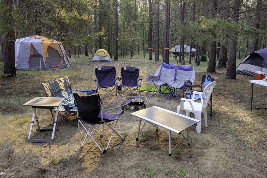 Camping chairs circled around a propane campfire with tents in the background