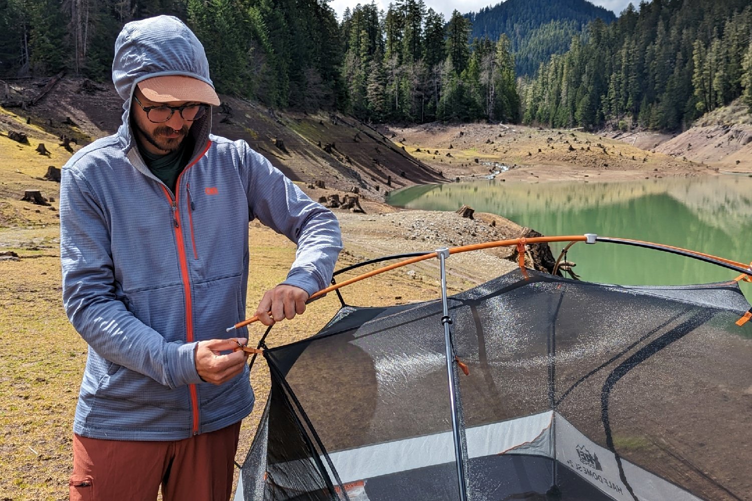 a backpacker in front of a reservoir attaching the poles to their tent