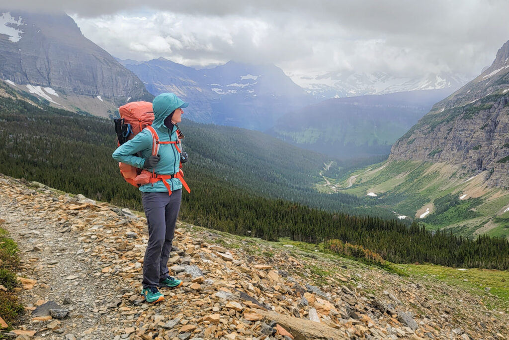 A backpacker wearing the Black Diamond Alpine Start Windbreaker while hiking in Glacier National Park in June