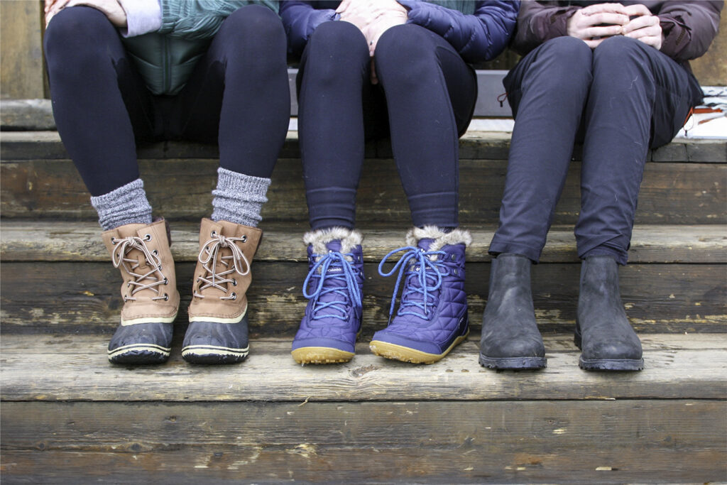 Closeup of three women's sitting on some steps in winter boots including the Sorel Slimpack III Lace & Columbia Minx Shorty III