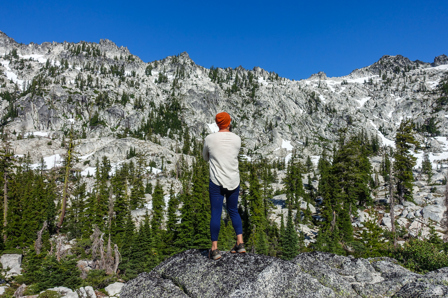 backpacker in his base layers looking a basin of granite and snow on a sunny day in the trinity alps