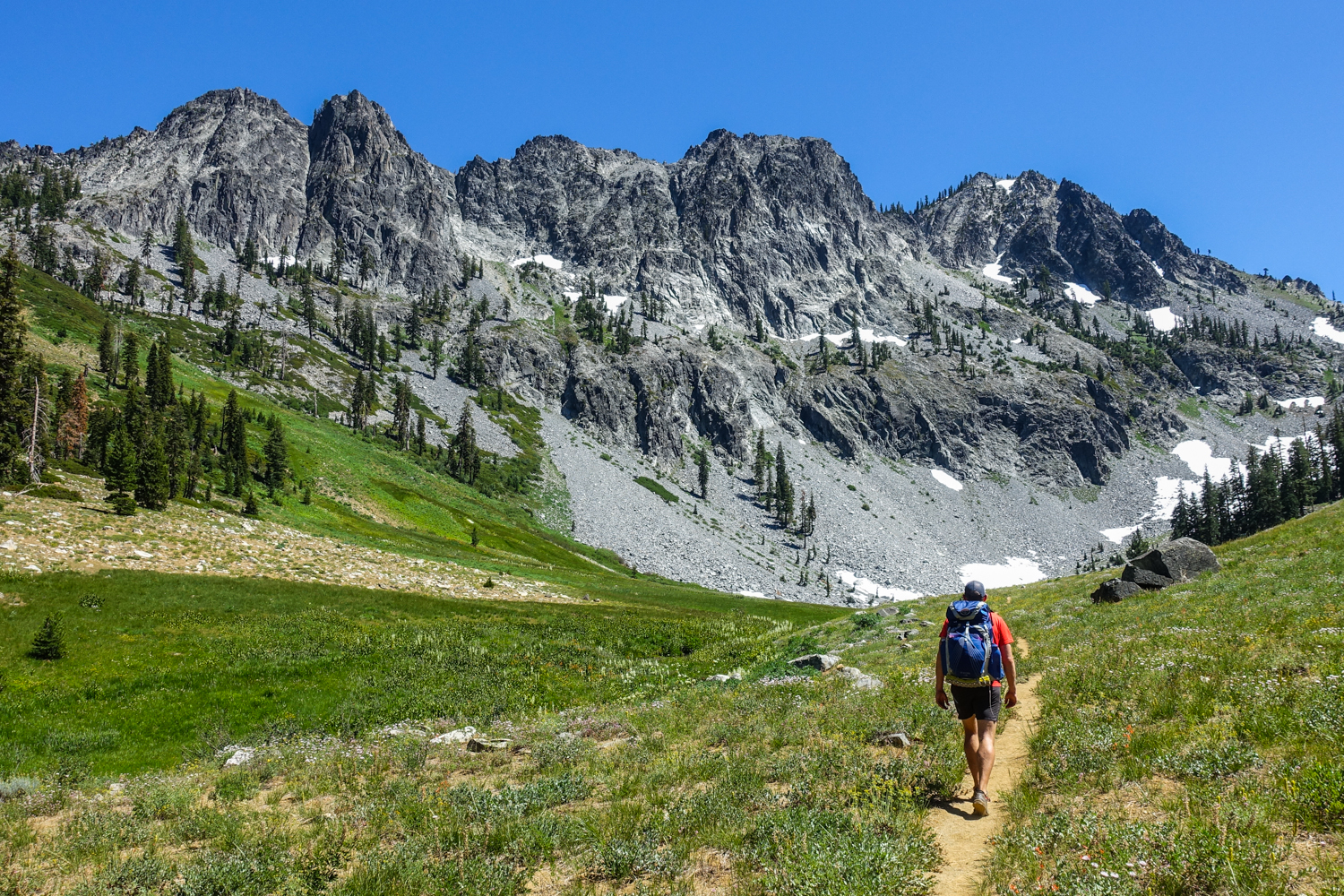 backpacker in the trinity alps walking toward a craggy granite ridge on a sunny day