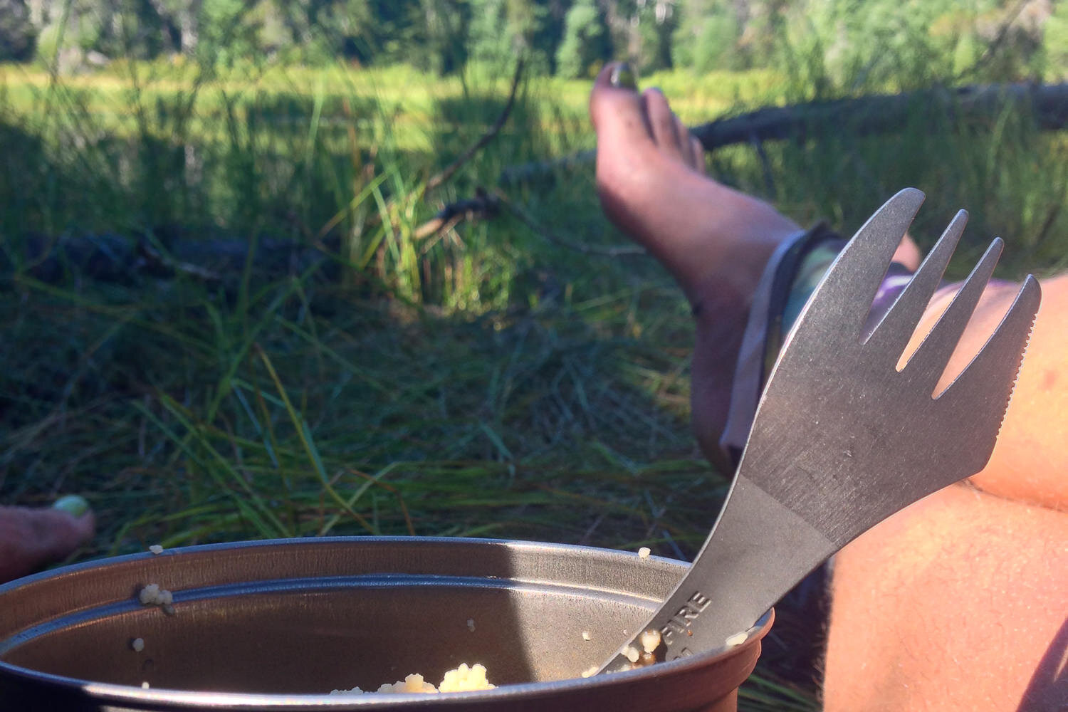 bare-foot thru-hiker stopping for a meal with a bowl of cous-cous and a spork for eating.