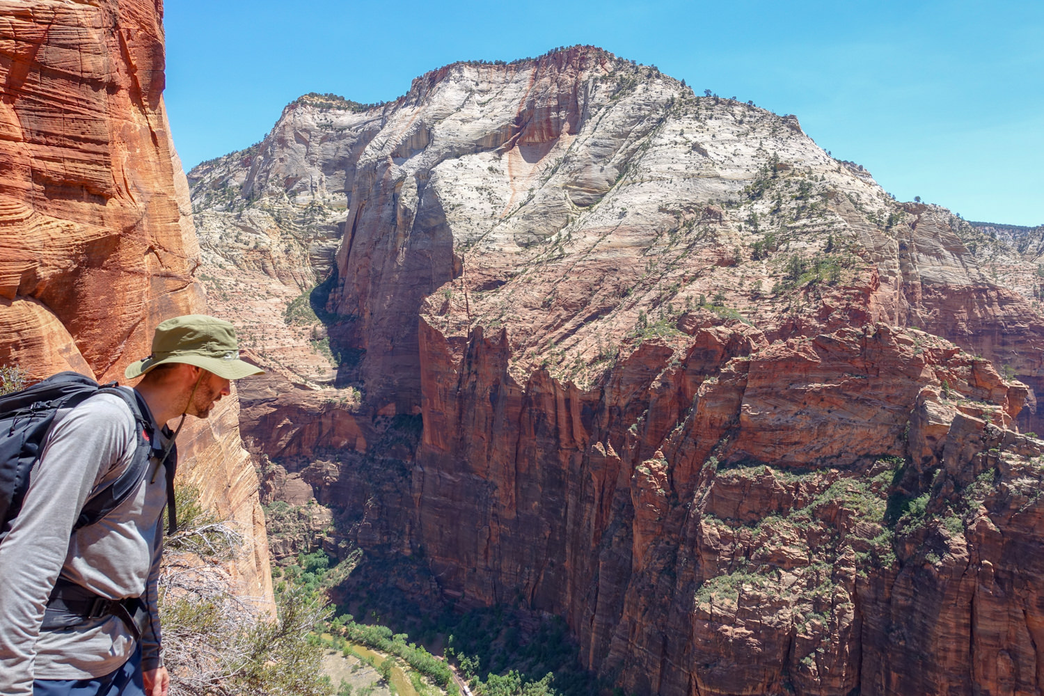 a backpacker on the trans-zion trek looks over a cliff into zion canyon