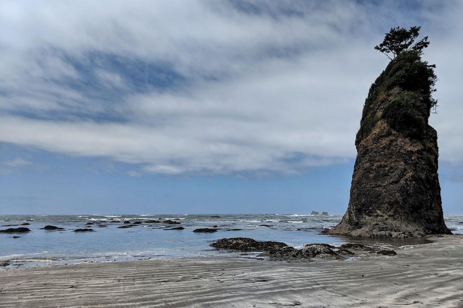 A rock juts up from shallow water and sand on an empty beach.