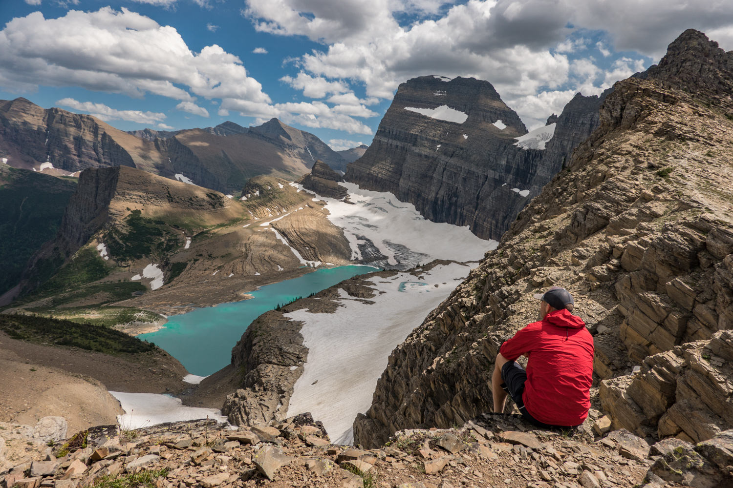 hiker seated above a glacier and its tarn in glacier national park