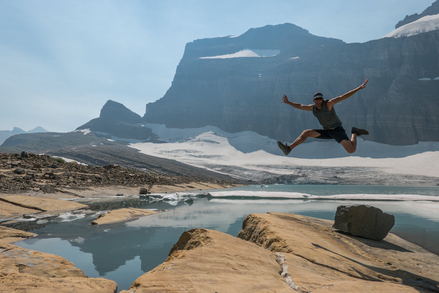 hiker mid-air posing in front of the grinnell glacier in glacier national park